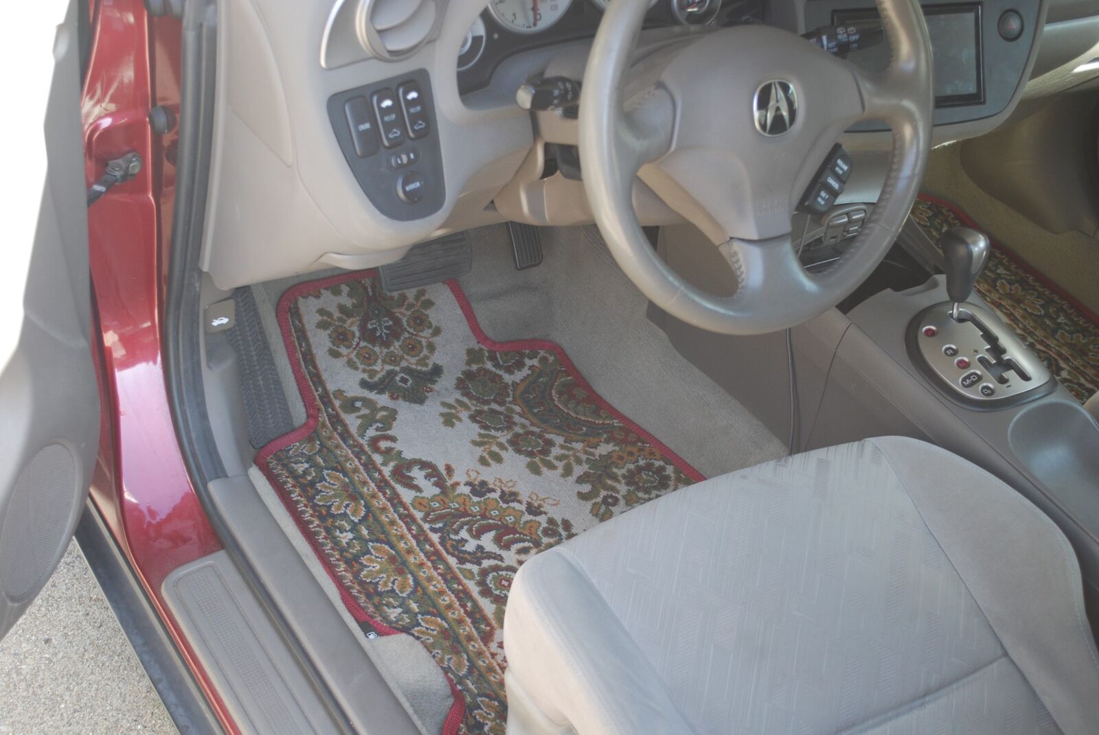 Finished Persian-rug floor mats with red binding in the driver's footwell, seen through the open door of the red Acura RSX