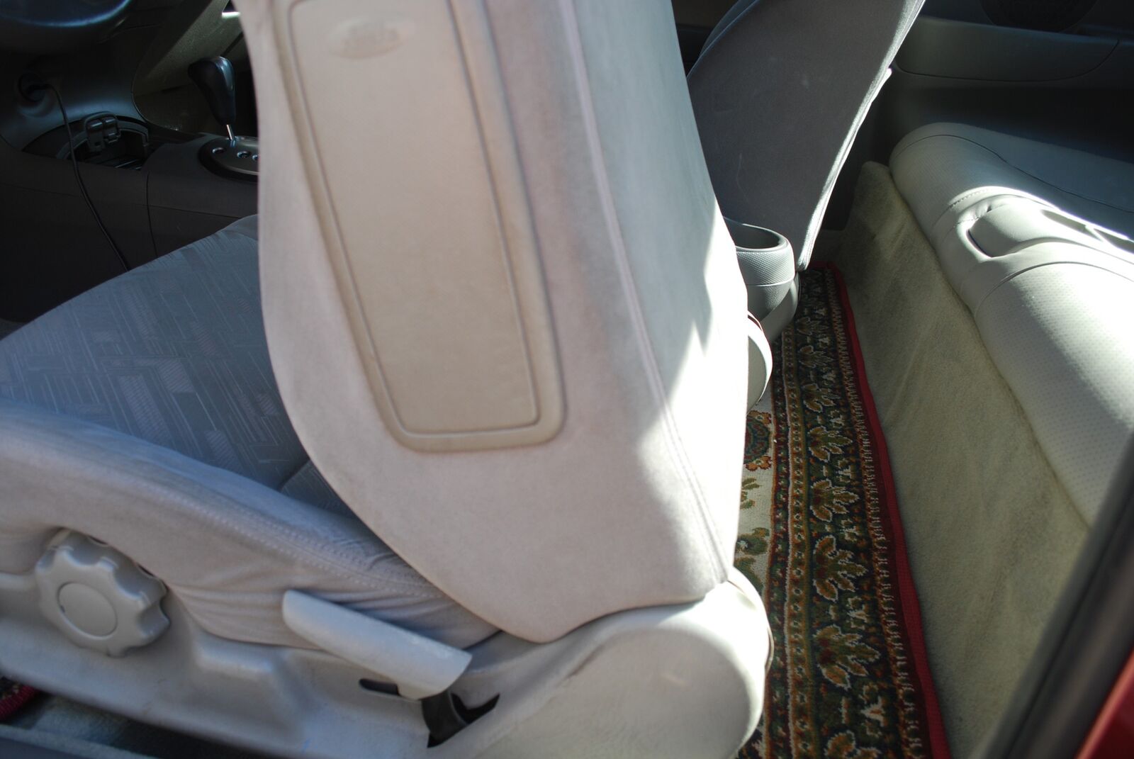 The rear floor mat in the same rug pattern, bound in red, seen past the folded-forward front seat