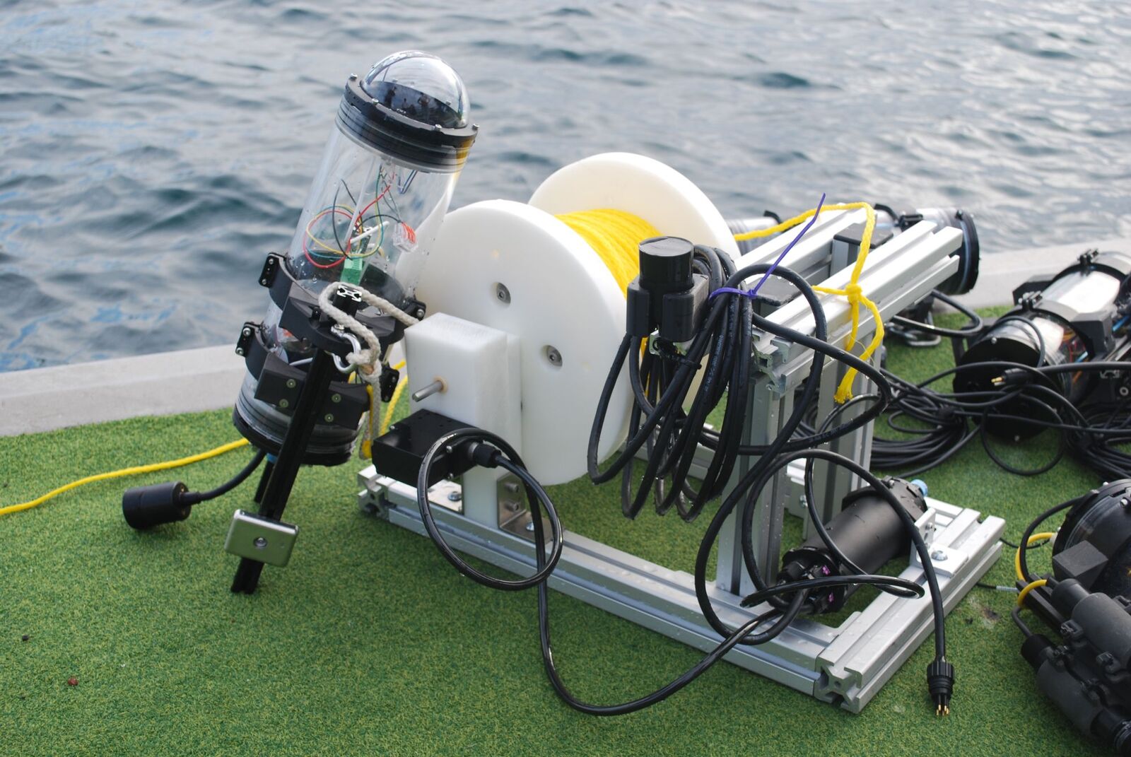 The reef monitoring hardware on a dock: a clear sensor housing, a tether reel and cabling on an aluminum frame
